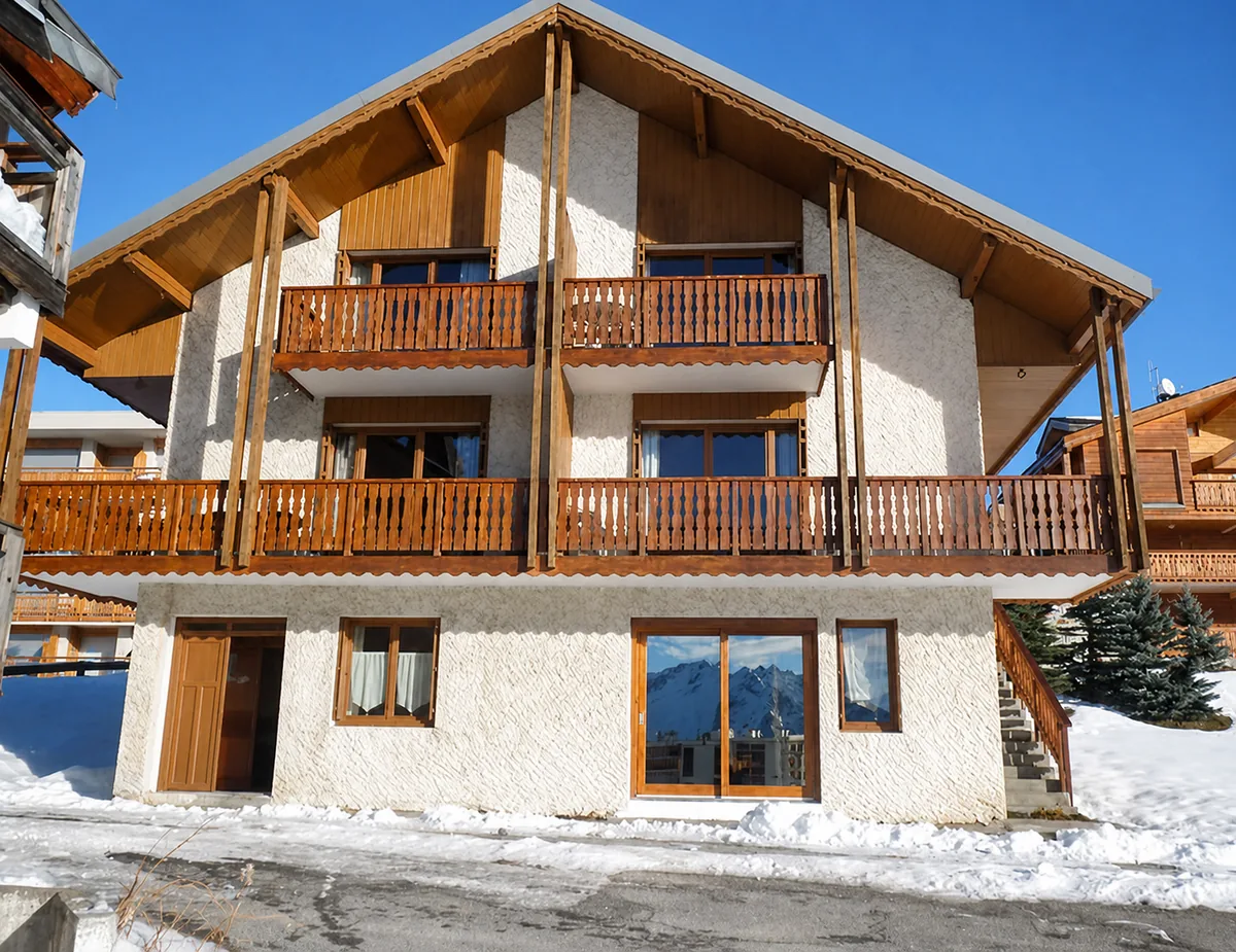 Le chalet L’Eau Vive, ses balcons en bois et la neige au pied de la façade